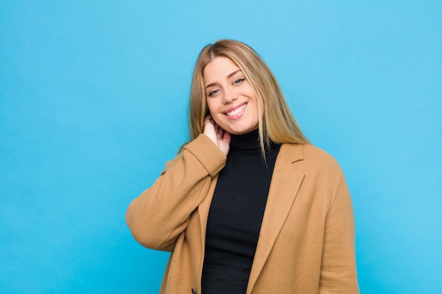 Young blonde woman laughing cheerfully and confidently with a casual, happy, friendly smile against wall