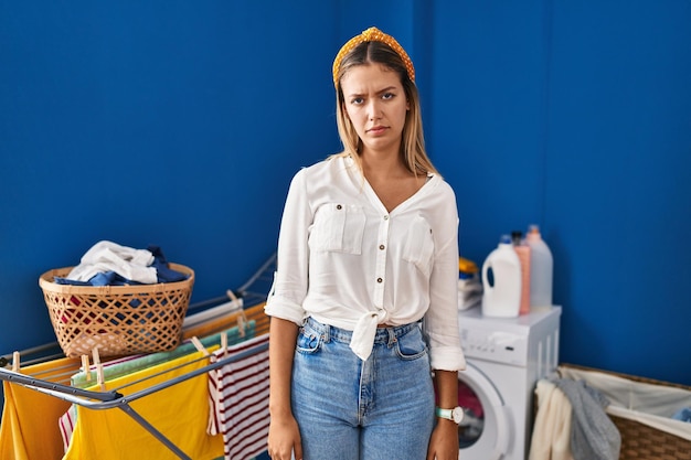 Photo young blonde woman at laundry room skeptic and nervous, frowning upset because of problem. negative person.