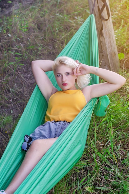 Young blonde woman lies in green tourist hammock on nature tourism summer vacation person