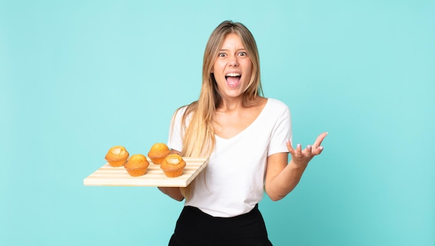 Young blonde woman looking angry, annoyed and frustrated and holding a muffins troy