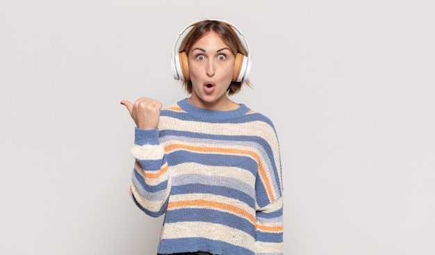 Young blonde woman looking astonished in disbelief, pointing at object on the side and saying wow, unbelievable