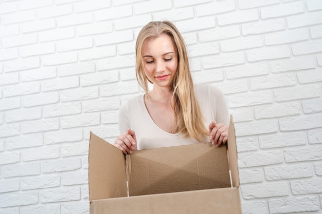 Young blonde woman looking in a box with white brick background