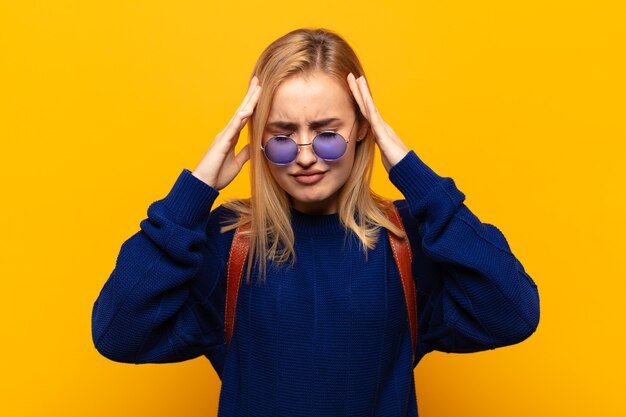 Young blonde woman looking concentrated, thoughtful and inspired, brainstorming and imagining with hands on forehead