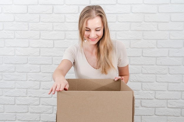 Молодая блондинка смотрит в коробку с доставкой на белом фоне