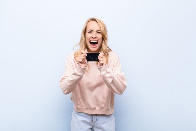 Young blonde woman looking desperate and frustrated, stressed, unhappy and annoyed, shouting and screaming using a smartphone