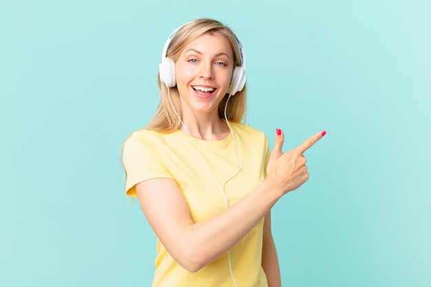 Young blonde woman looking excited and surprised pointing to the side and listening music.