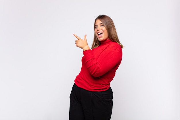 Young blonde woman looking excited and surprised pointing to the side and upwards to copy space