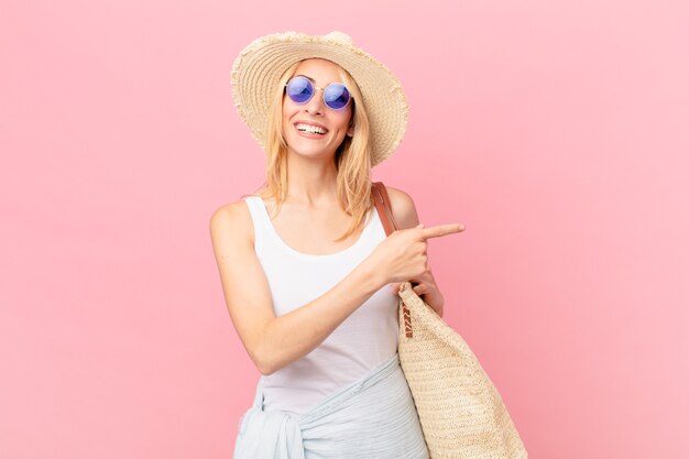 Young blonde woman looking excited and surprised pointing to the side