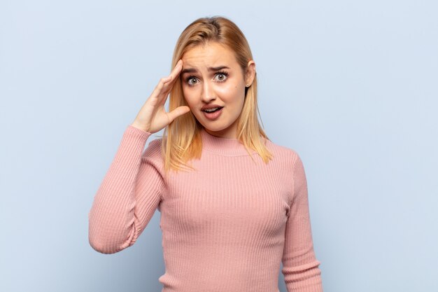 Young blonde woman looking happy, astonished and surprised, smiling and realizing amazing and incredible good news