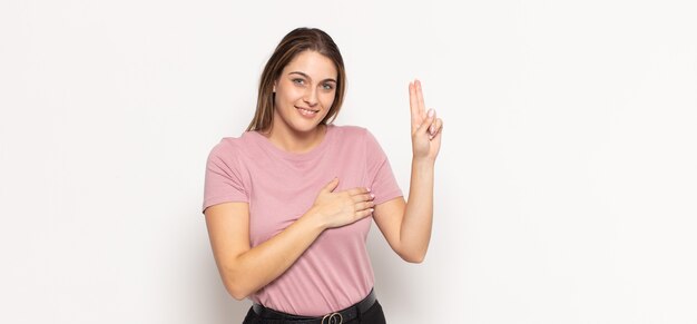 Young blonde woman looking happy, confident and trustworthy, smiling and showing victory sign, with a positive attitude