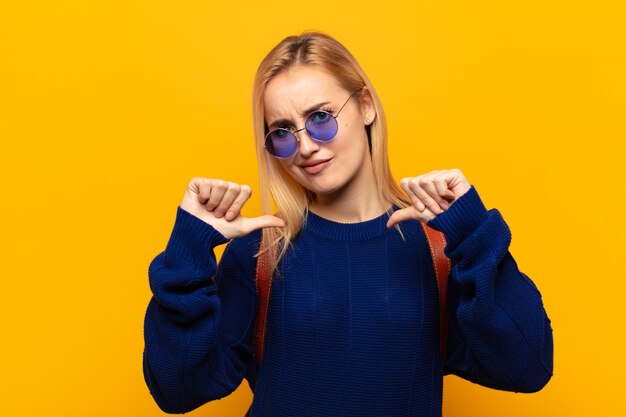 young blonde woman looking sad, disappointed or angry, showing thumbs down in disagreement, feeling frustrated