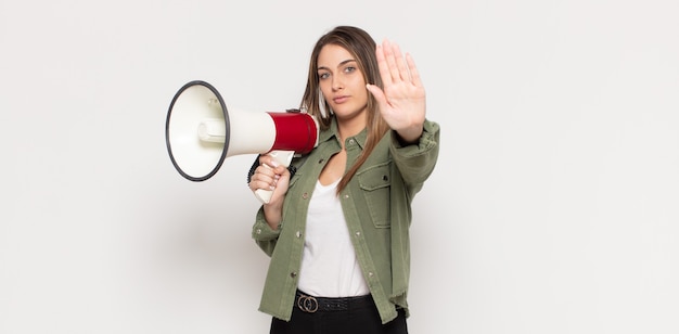 Young blonde woman looking serious, stern, displeased and angry showing open palm making stop gesture