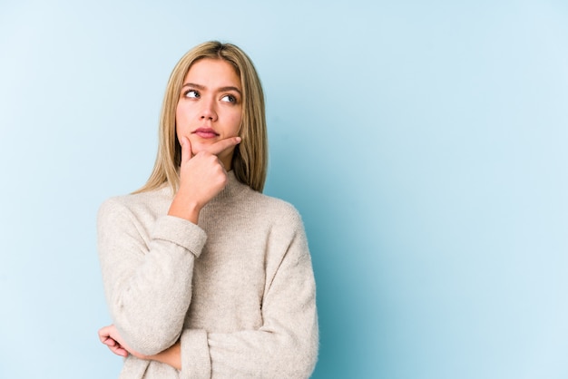 Young blonde woman looking sideways with doubtful and skeptical expression