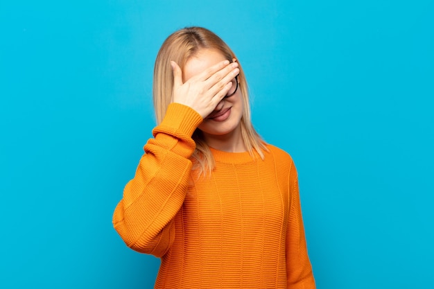 Young blonde woman looking stressed, ashamed or upset, with a headache, covering face with hand