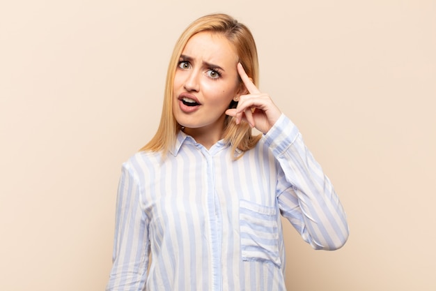 Young blonde woman looking surprised, open-mouthed, shocked, realizing a new thought, idea or concept