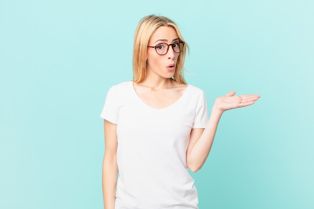 young blonde woman looking surprised and shocked, with jaw dropped holding an object