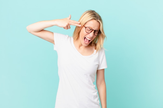 Young blonde woman looking unhappy and stressed, suicide gesture making gun sign