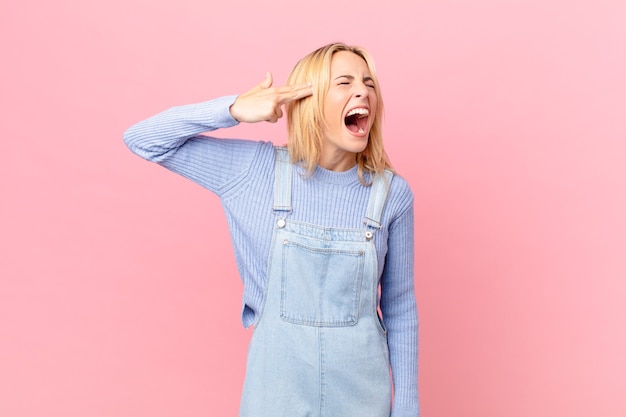 young blonde woman looking unhappy and stressed, suicide gesture making gun sign