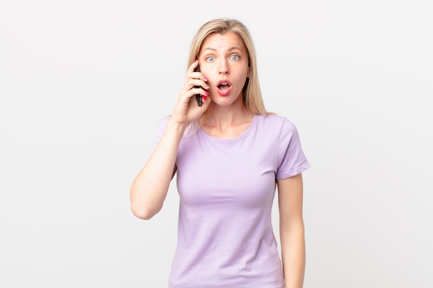 Young blonde woman looking very shocked or surprised and calling with a smart phone