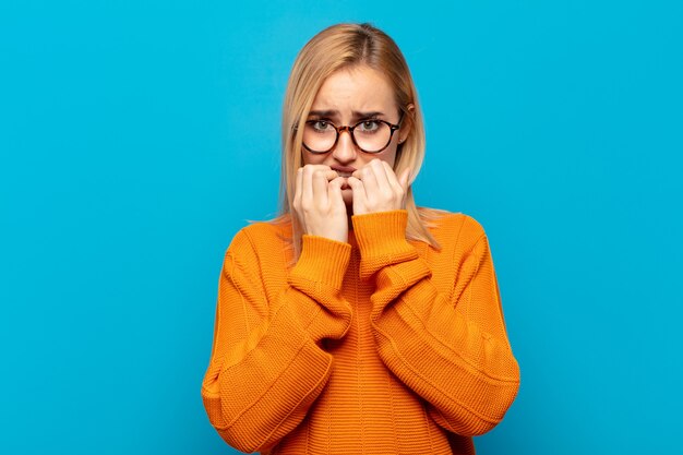 Young blonde woman looking worried, anxious, stressed and afraid, biting fingernails and looking to lateral copy space