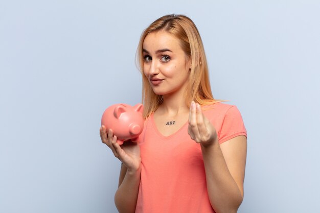 Young blonde woman making capice or money gesture, telling you to pay your debts!