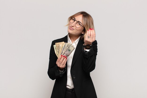 young blonde woman making capice or money gesture, telling you to pay your debts!