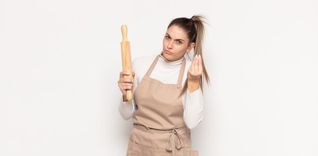 Young blonde woman making capice or money gesture, telling you to pay your debts!