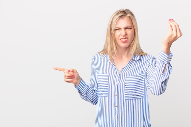 Young blonde woman making capice or money gesture telling you to pay