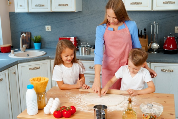 Young blonde woman, mother and her kids having fun while cooking dough 