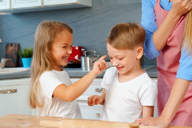 Young blonde woman, mother and her kids having fun while cooking dough