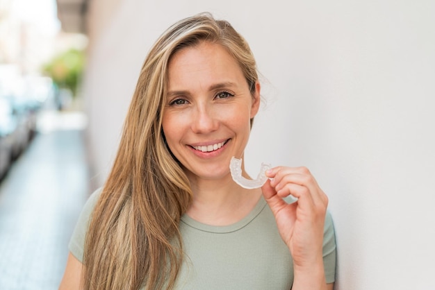 Photo young blonde woman at outdoors holding invisible braces