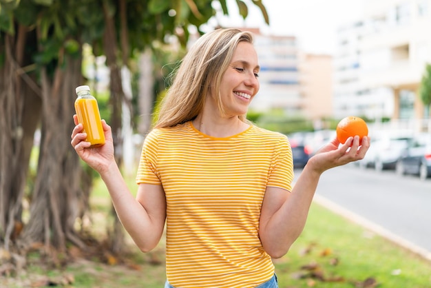 オレンジとオレンジジュースを握っている屋外の若い金の女性