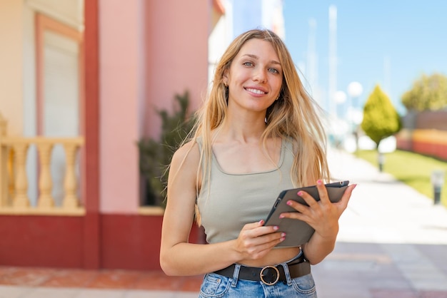 屋外で幸せな表情でタブレットを持っている若いブロンドの女性