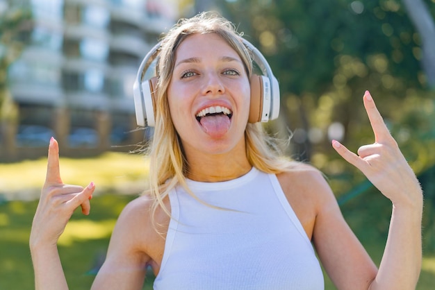 Young blonde woman at outdoors listening music making rock gesture