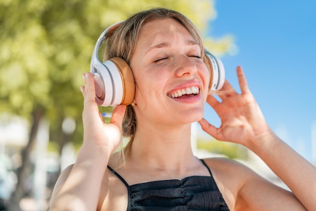 Young blonde woman at outdoors listening music and singing