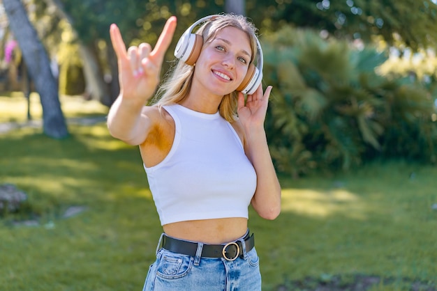 Young blonde woman at outdoors listening music and singing