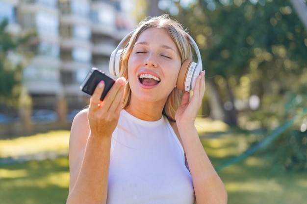 Young blonde woman at outdoors listening music with a mobile and singing