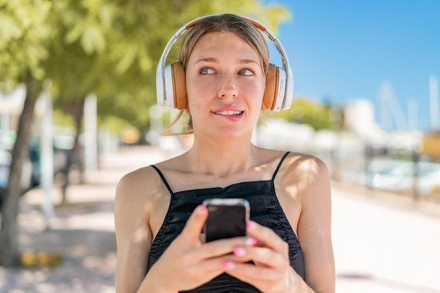 Foto giovane donna bionda alla musica d'ascolto all'aperto con un cellulare e un pensiero