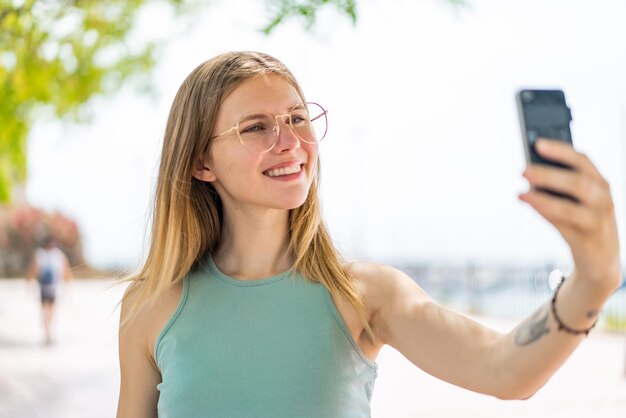 Young blonde woman at outdoors making a selfie with mobile phone