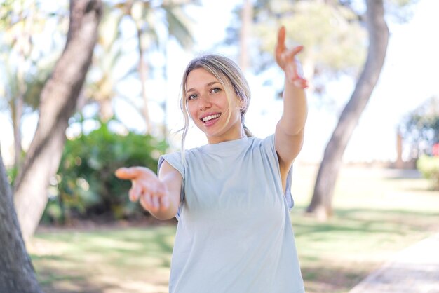 Photo young blonde woman at outdoors presenting and inviting to come with hand