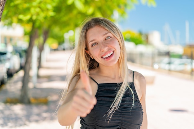 Young blonde woman at outdoors with thumbs up because something good has happened