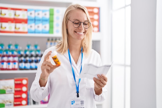 Фото Молодая блондинка-фармацевт держит бутылку с таблетками и читает рецепт в аптеке