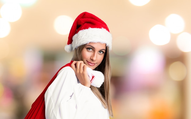 Young blonde woman picking up a bag full of presents in christmas holidays on unfocused wall