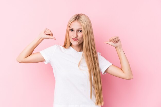 Young blonde woman on pink wall feels proud and self confident, example to follow.