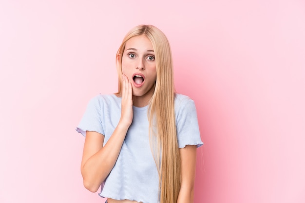 Young blonde woman on pink wall scared and afraid.