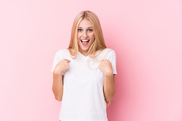 La giovane donna bionda sulla parete rosa ha sorpreso indicare con il dito, sorridendo ampiamente.