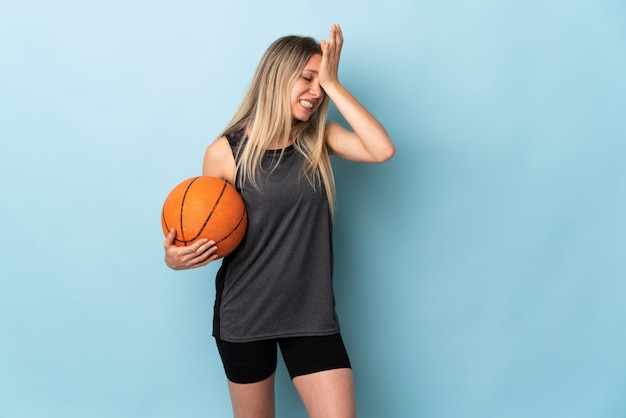 Young blonde woman playing basketball isolated on blue wall having doubts with confuse face expression