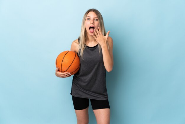 Young blonde woman playing basketball isolated on blue wall with surprise facial expression