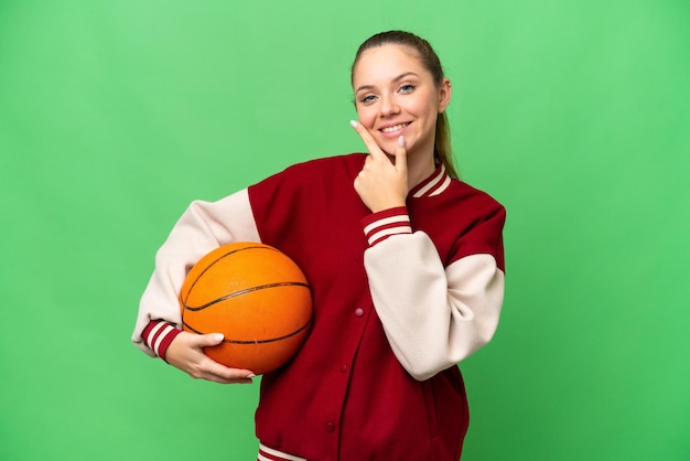 Young blonde woman playing basketball over isolated chroma key background happy and smiling