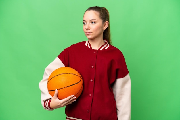 Молодая блондинка играет в баскетбол на изолированном фоне хроматического ключа, глядя в сторону